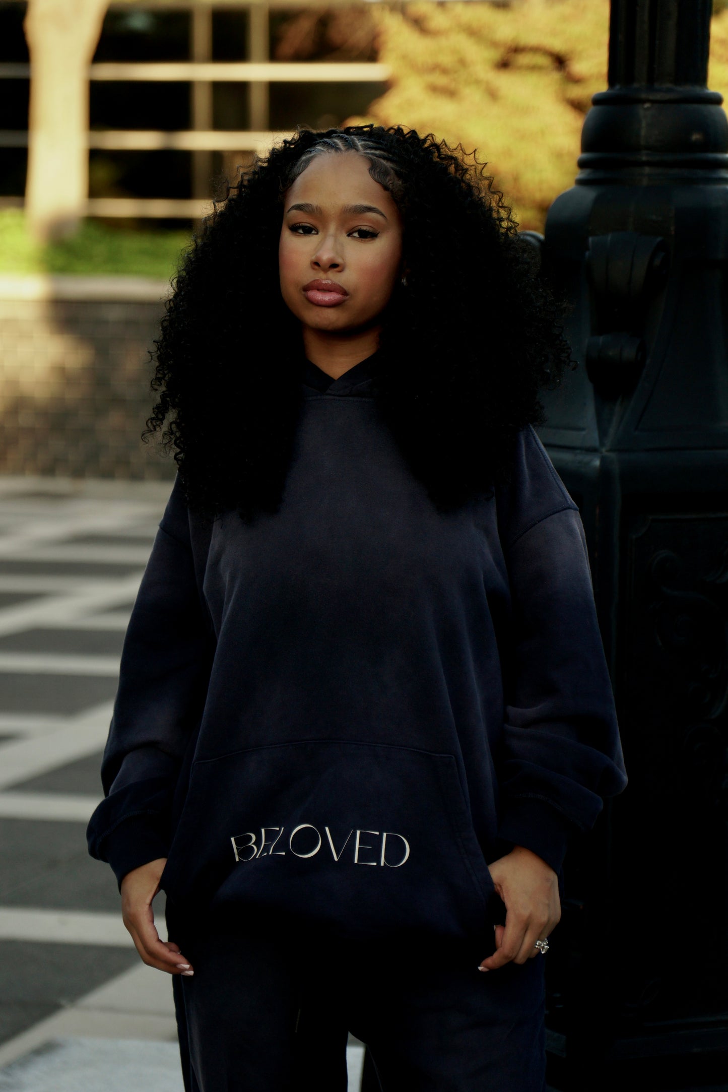 Person wearing a navy blue hoodie with 'BELOVED' text, standing outdoors.