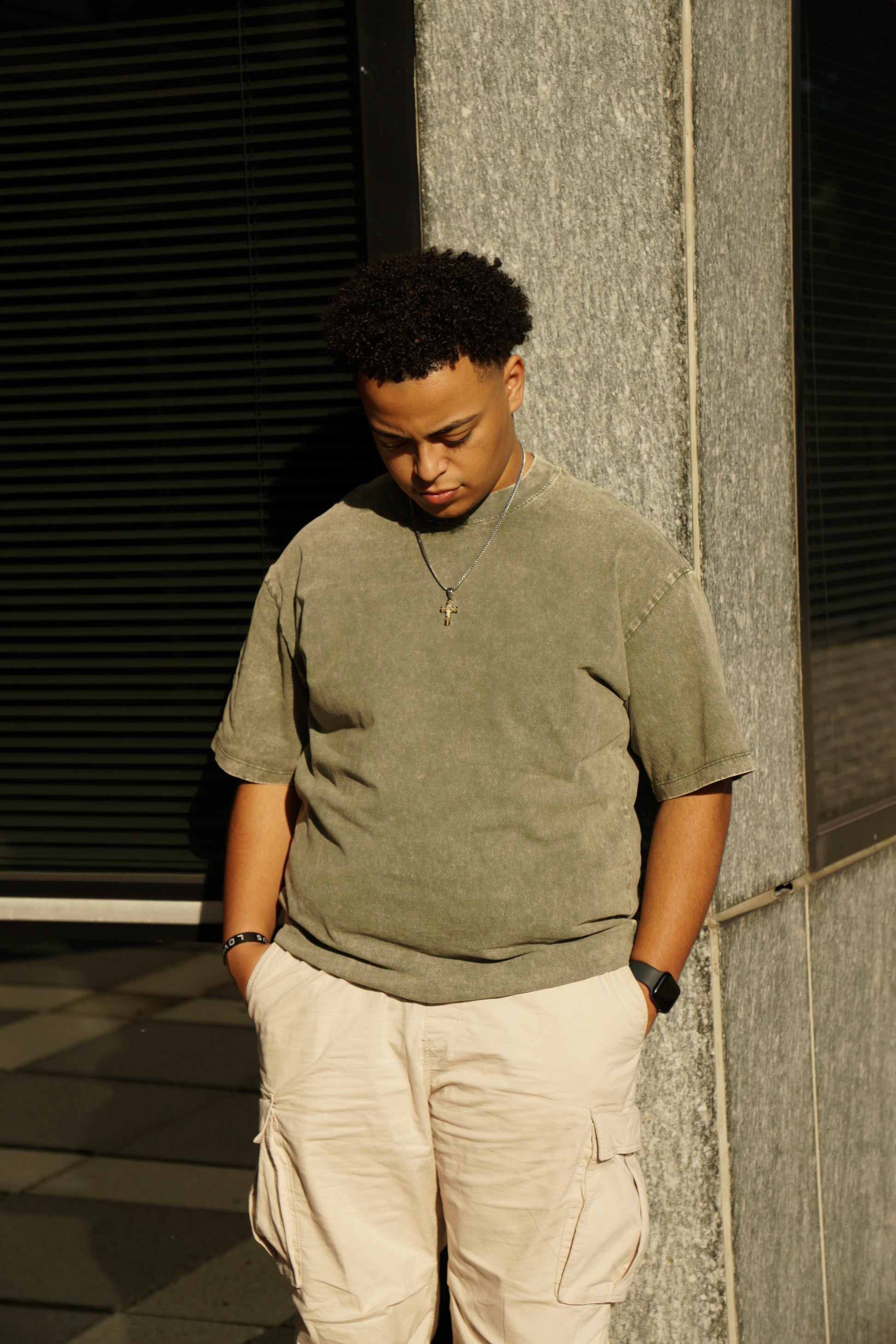 hype4holy christian apparel mtc streetwear oversized faded green t shirt, model picture, front | Man wearing a green shirt and beige pants standing against a textured wall.