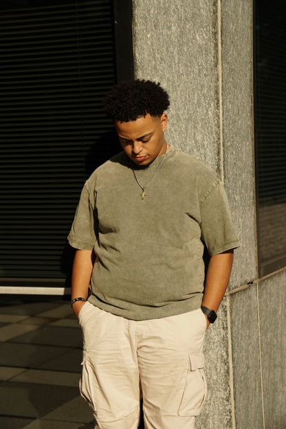 hype4holy christian apparel mtc streetwear oversized faded green t shirt, model picture, front | Man wearing a green shirt and beige pants standing against a textured wall.