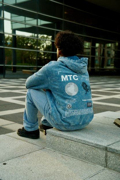 hype4holy christian apparel streetwear oversized faded hoodie blue color model picture back | Person wearing a blue hoodie with 'MTC' design sitting on steps outdoors.